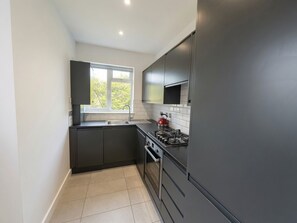 A modern kitchen with dark cabinetry, a gas stove, and a built-in microwave. - Stylish 2BR Home with Outdoor Dining/ Social Area (London)