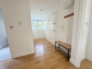 A hallway with wooden flooring, white walls, and a bench. There are doors and a window at the end of the hallway. - Stylish 2BR Home with Outdoor Dining/ Social Area (London)