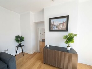 Ein modernes Wohnzimmer mit einem Holzkonsolentisch, zwei Topfpflanzen und einem gerahmten Stadtbild an der Wand.