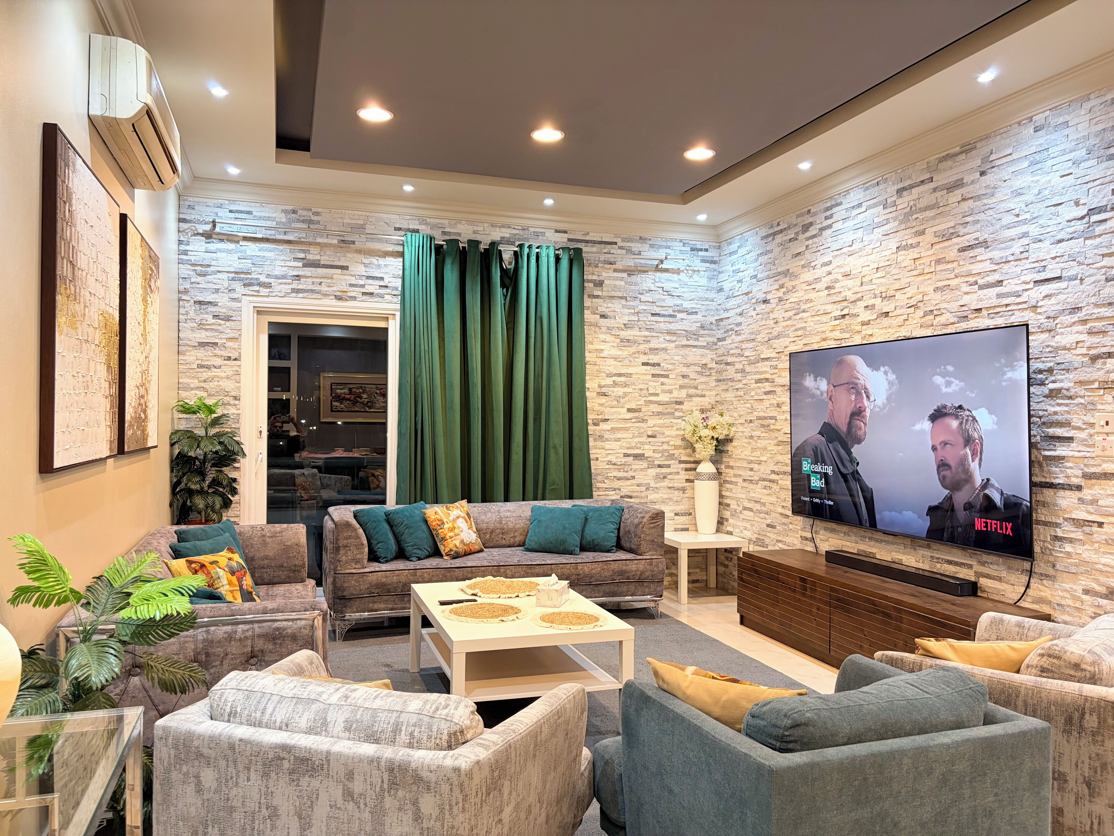 A modern living room with a stone-textured wall, a flat-screen TV, and a cozy seating arrangement.