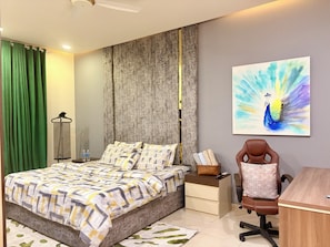 Ein Schlafzimmer mit einem Bett, einem Schreibtisch, einem Stuhl, einem Wandbild und einem grünen Vorhang.