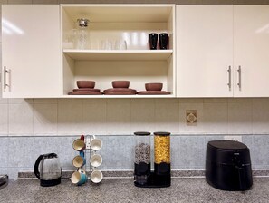 Eine Küche mit weißen Schränken, einer Kaffeemaschine, einem Wasserkocher, einem Reiskocher und einem Gewürzregal.
