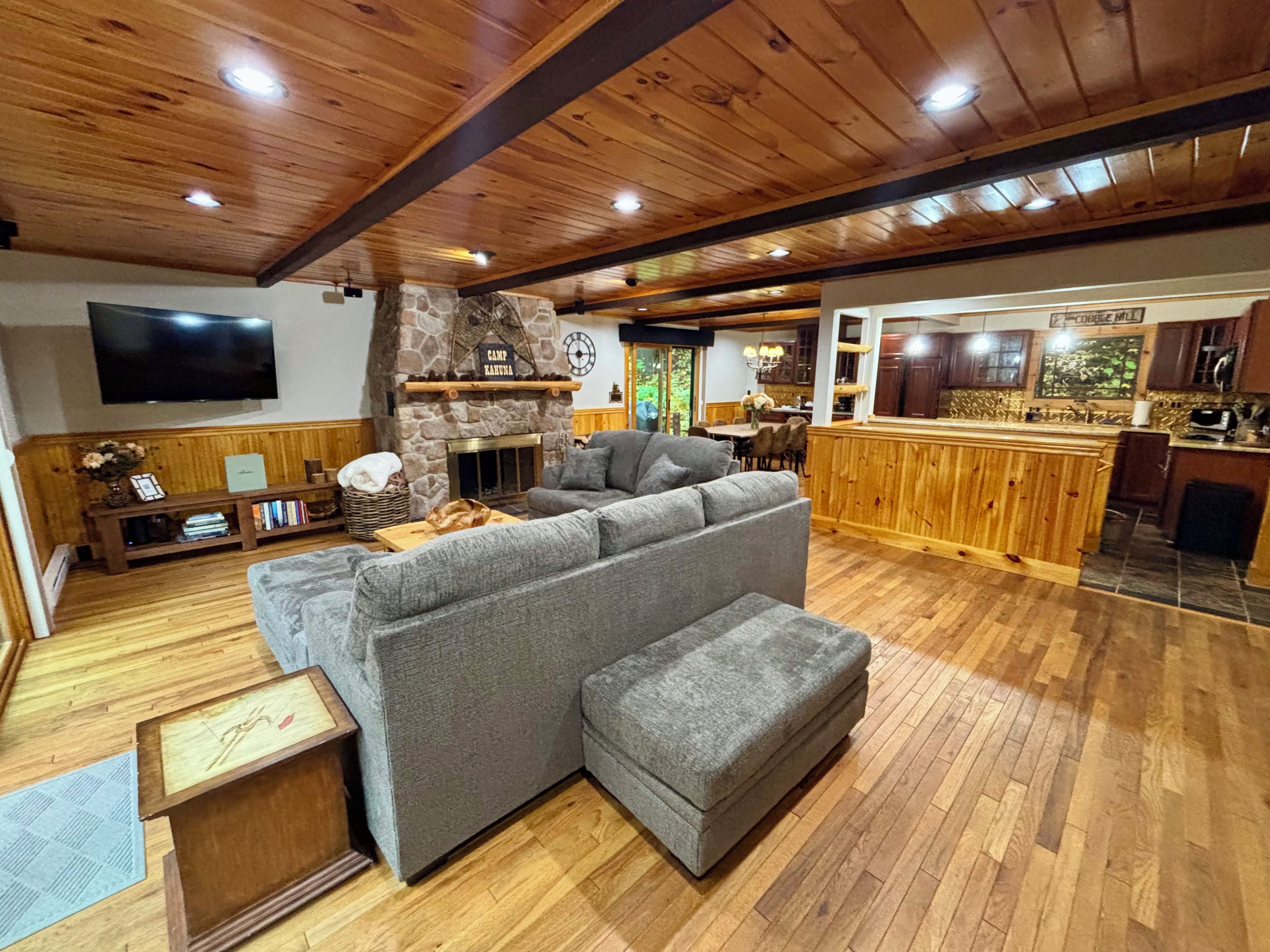 Un salon chaleureux avec un canapé d’angle, une cheminée en pierre et un plafond en bois.