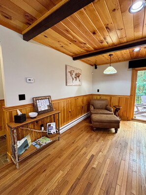 A wooden-floored room with a sofa, a small table with a globe and a framed menu, and a hanging light fixture. - Camp Kahuna - Near Mirror Lake - Dog Friendly (Lake Placid)