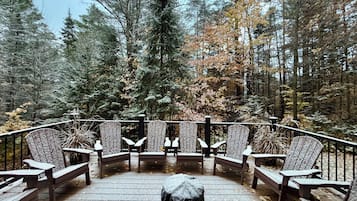 A deck with wooden chairs and benches, surrounded by a forest with tall trees.