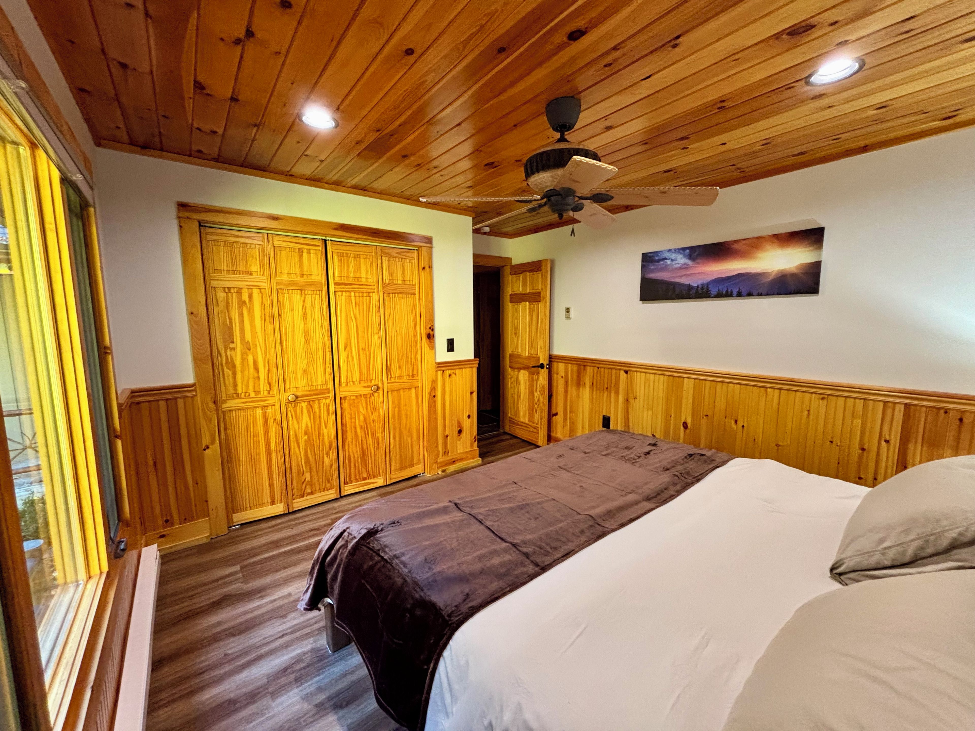 Un dormitorio con techo de madera, una cama con colcha marrón, un cuadro en la pared y un armario de madera.