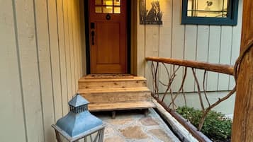 Une porte d’entrée en bois, un paillasson, une lanterne et une citrouille rouge sur un porche dallé de pierres.