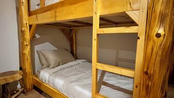 Een stapelbed met houten frame, een klein krukje en een betegelde vloer.