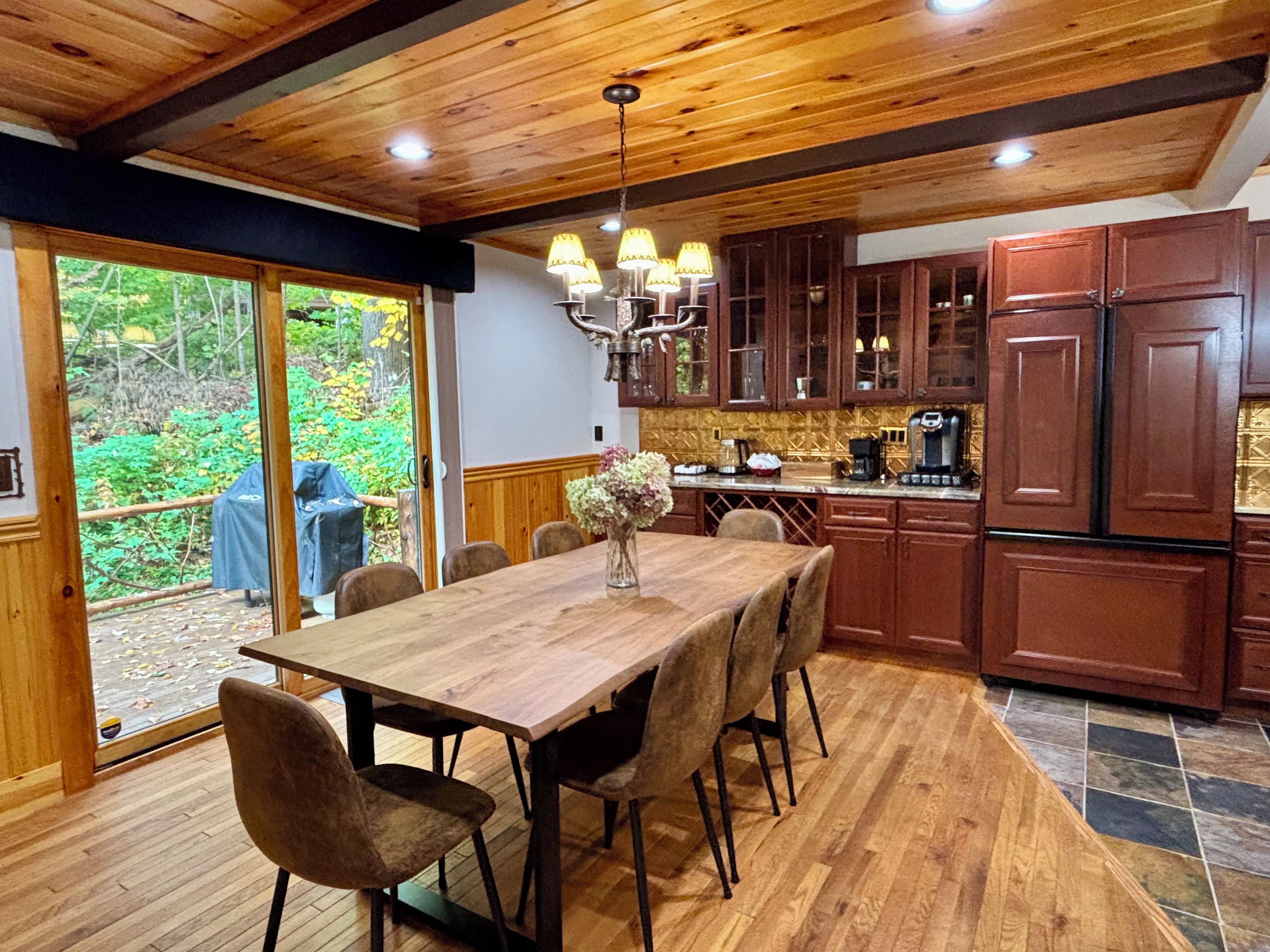 Une table à manger en bois, des chaises, un lustre et une vue sur l’extérieur grâce à une porte-fenêtre coulissante.