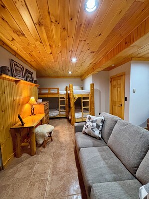 A cozy room with wooden bunk beds, a sofa, a desk with a lamp, and a small chair. - Camp Kahuna - Near Mirror Lake - Dog Friendly (Lake Placid)