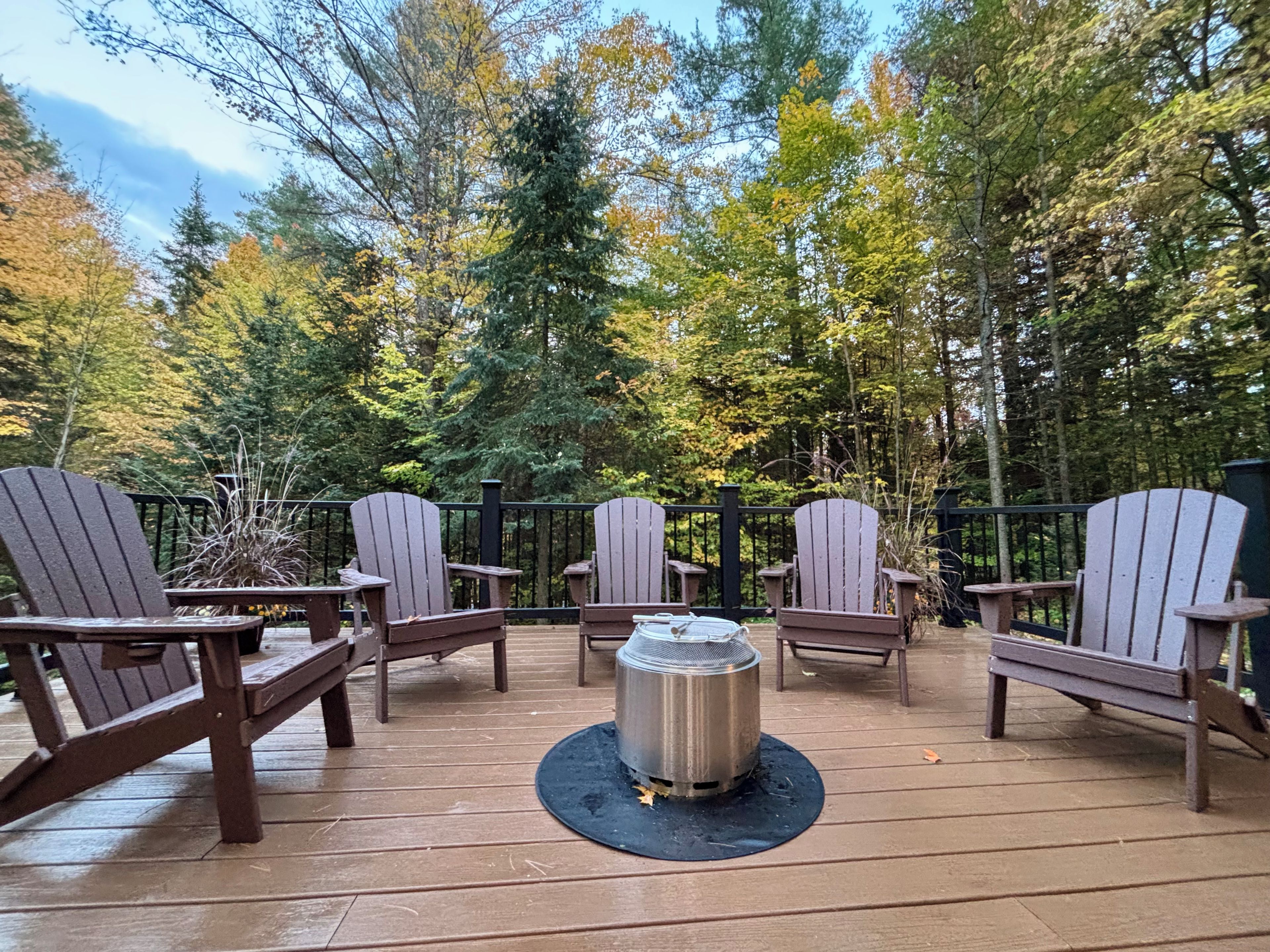 Une terrasse avec des chaises en bois et un radiateur en métal, entourée d’arbres.