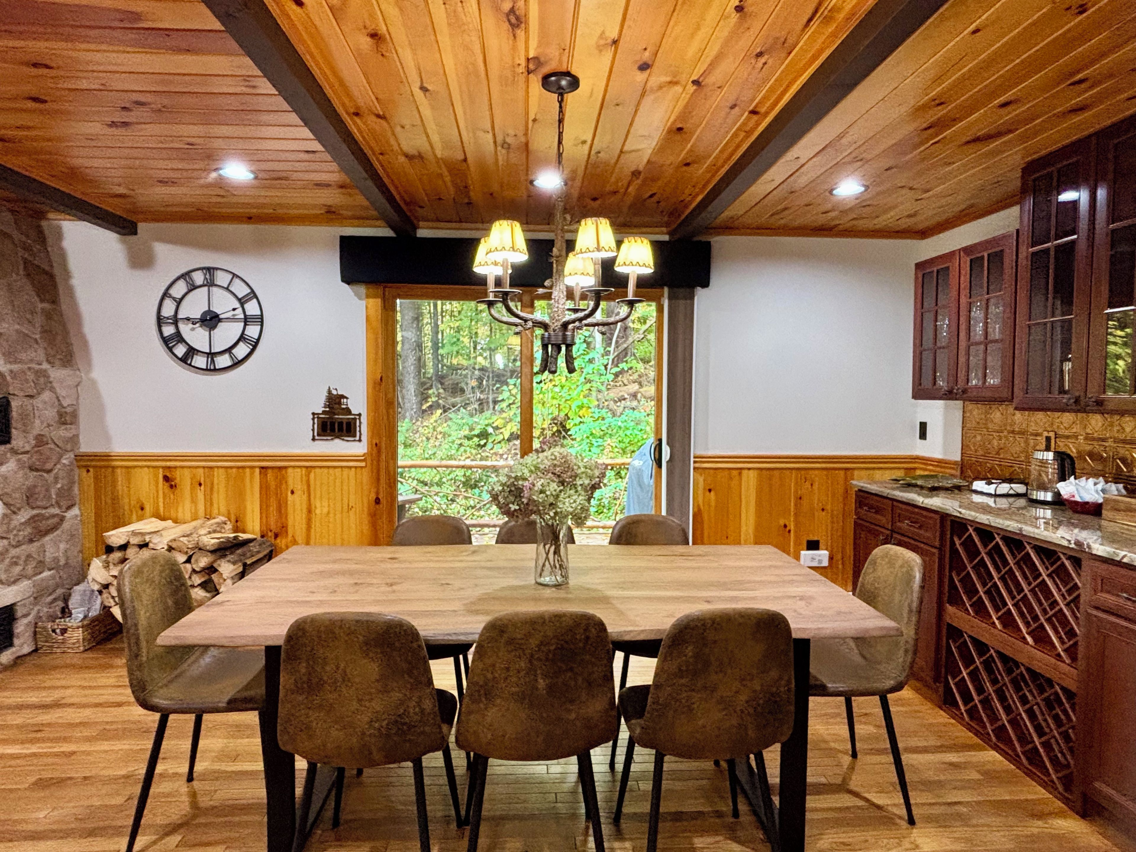 Une table à manger en bois, des chaises, un lustre et une horloge au mur.