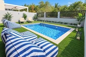 Ein Schwimmbecken mit gefliestem Deck, umgeben von Gras und Kübelpflanzen.