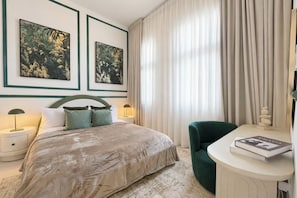Ein Hotelzimmer mit einem Bett, zwei Nachttischen, einem Schreibtisch, einem Stuhl und Vorhängen.