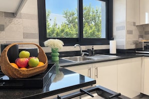 Een moderne keuken met een zwart aanrecht, een RVS spoelbak en een raam met uitzicht op bomen.
