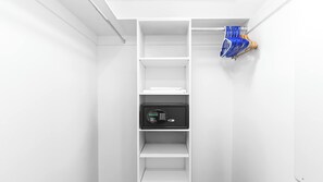 A white closet with shelves, a black safe, and a blue and white hanging rack. - City & Marina Views 2BR APT w/ Home‑Style Comforts (Hallandale Beach)