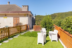A house with a stone facade, a wooden fence, and a grassy yard with two white wicker chairs. - A unique and charming attic apartment, thoughtfully designed and fully equipped (Piazza)