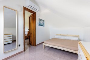 Een slaapkamer met een bed, een houten garderobe, een spiegel, een airconditioning en een schilderij aan de muur.