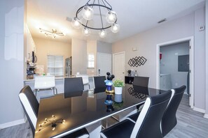 A modern dining area with a black table, white chairs, and a decorative plant centerpiece. - Prime Location Bella Vida Pool Retreat Near Disney (Kissimmee)