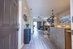 A modern kitchen with a marble countertop, a dining area with a sofa and table, and a hallway with a door. - Prime Location Bella Vida Pool Retreat Near Disney (Kissimmee)