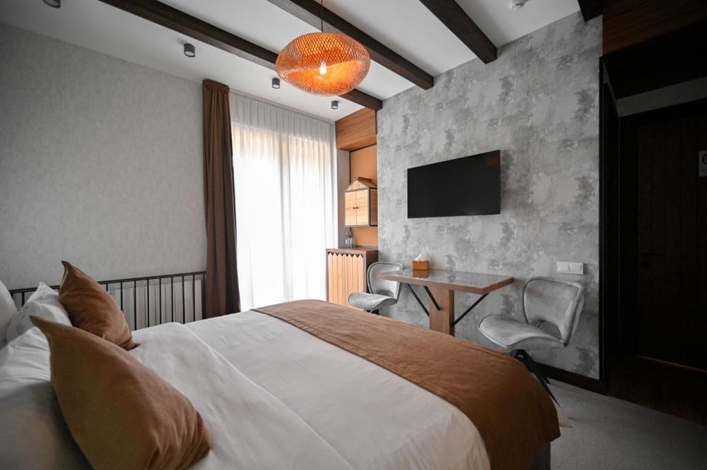 Una habitación de hotel moderna con una cama grande, un escritorio, una silla y un televisor fijado a la pared.