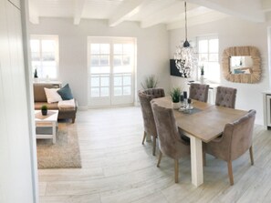 A dining area with a wooden table and upholstered chairs, a chandelier, and a large window with a view. - Little Baked Apple (Wrixum)