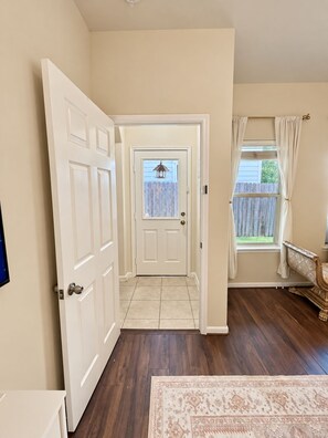 A hallway with a door leading to a backyard, a window with curtains, and a rug on the floor. - Elegant Private Master Bedroom Suite • Private Spa Bath, Soaking Tub & Patio (Houston)