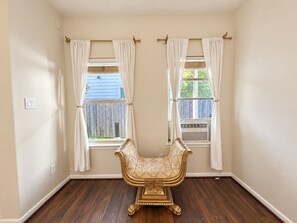 A room with two windows, a patterned armchair, and a wooden floor. - Elegant Private Master Bedroom Suite • Private Spa Bath, Soaking Tub & Patio (Houston)