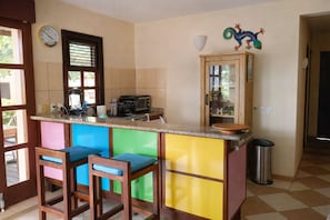 A kitchen with a bar area, a clock, and a decorative lizard on the wall. - Poco Poco Villa at Blue Bay Resort | Pool, Beach & Golf (Willemstad)
