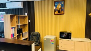 A room with a wooden bookshelf, a desk, a chair, a refrigerator, and a microwave. - THE PARADISE INN PATTAYA (Muang Pattaya)