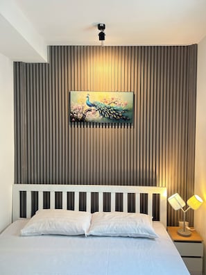 A bedroom with a bed, a wall-mounted painting of a peacock, and a nightstand with a lamp. - THE PARADISE INN PATTAYA (Pattaya)