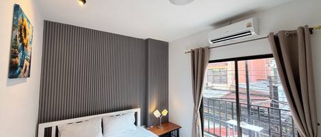 A hotel room with a bed, a bedside table with a lamp, a painting on the wall, and a view of the outside balcony.