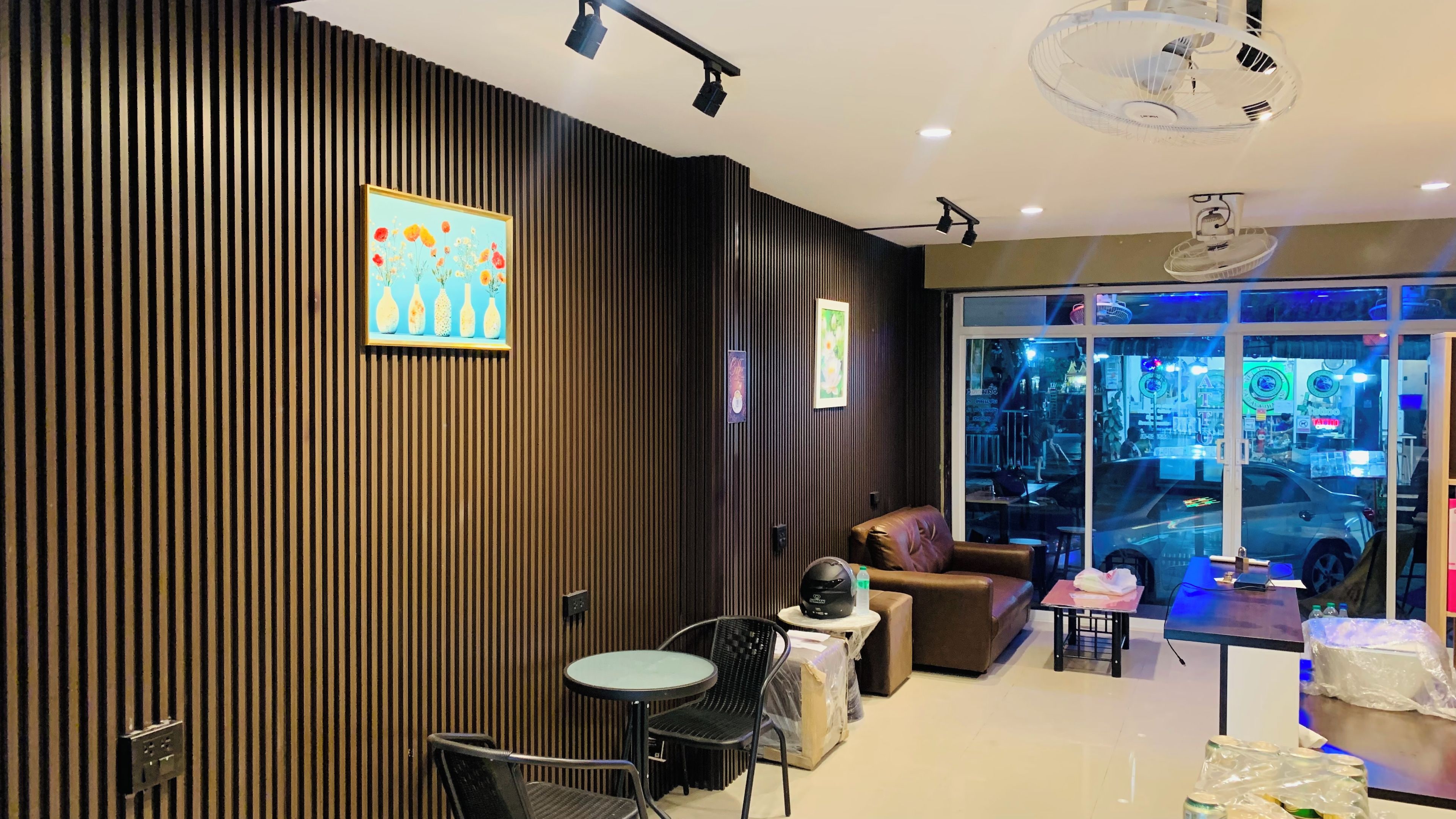 Ein modernes Interieur mit einer Holzwandverkleidung, einem Gemälde, einer Couch, einem Tisch und Blick auf die Straße durch große Fenster.