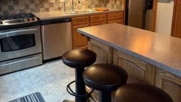 A kitchen with wooden cabinets, a stainless steel stove, a refrigerator, and a bar stool.
