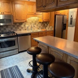 Une cuisine avec des meubles en bois, une cuisinière en acier inoxydable, un réfrigérateur et un tabouret de bar.