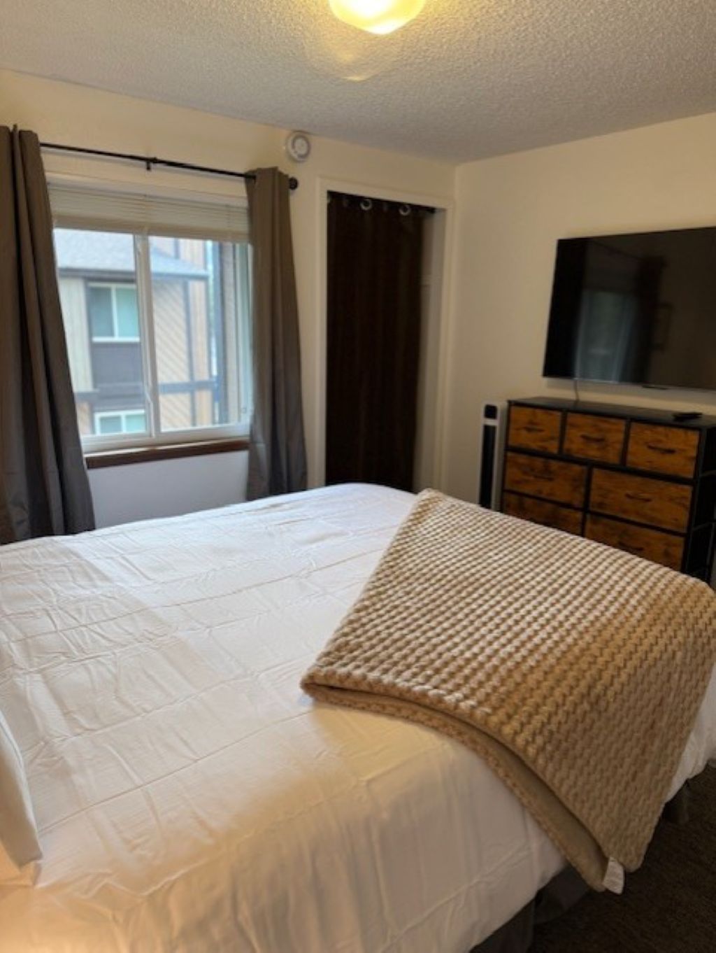 Quarto com cama, televisão sobre uma cômoda e janela com cortinas.