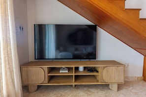 A wooden entertainment unit with a flat-screen TV, a white speaker, and a gaming console. - Luxury Beachfront Apartment in Sosua! (Sosúa)