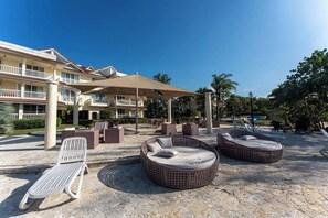 A resort with outdoor seating, including wicker chairs and a bench, under a shaded area. - Luxury Beachfront Apartment in Sosua! (Sosúa)