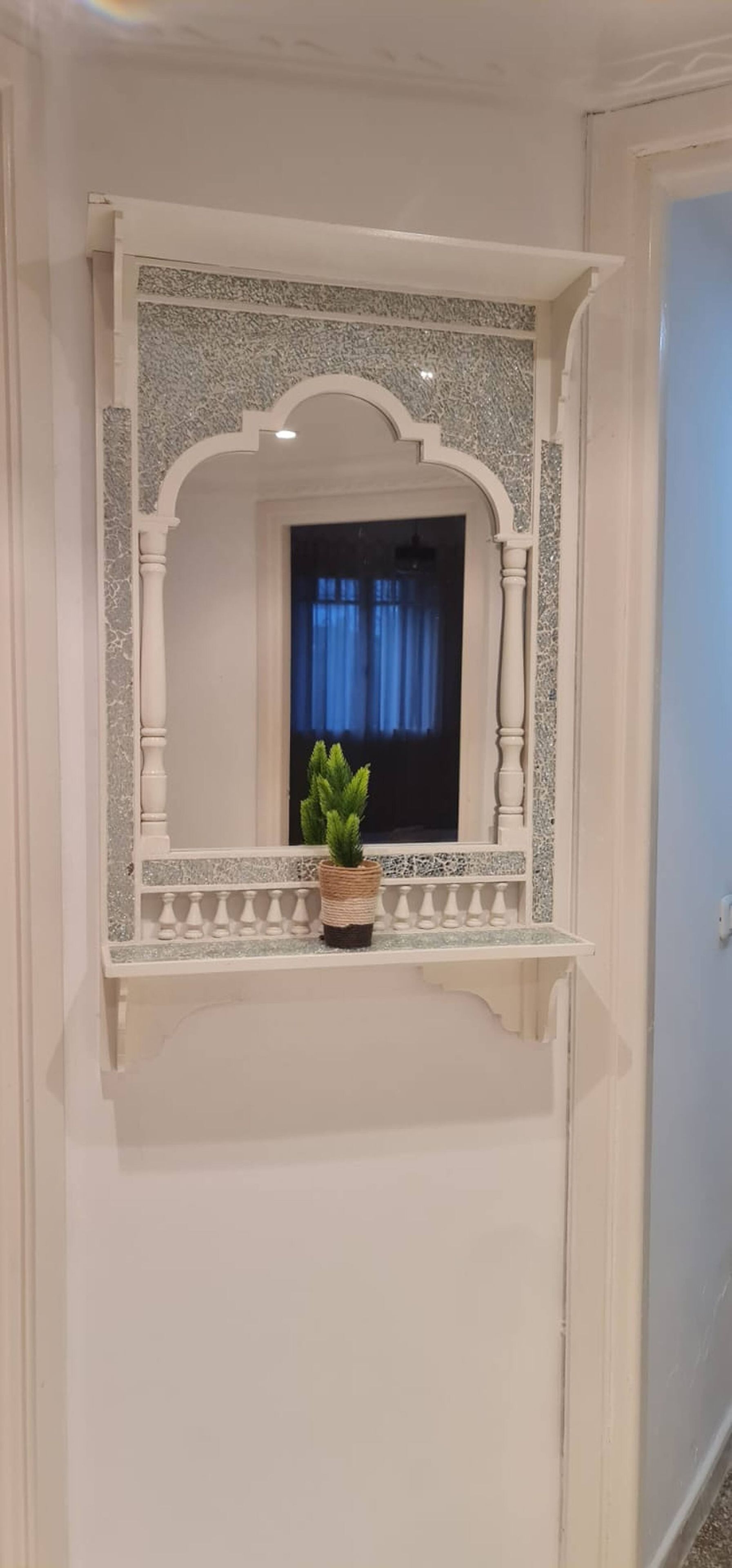 Una stanza con uno specchio decorativo, una pianta in vaso e una finestra con tende.