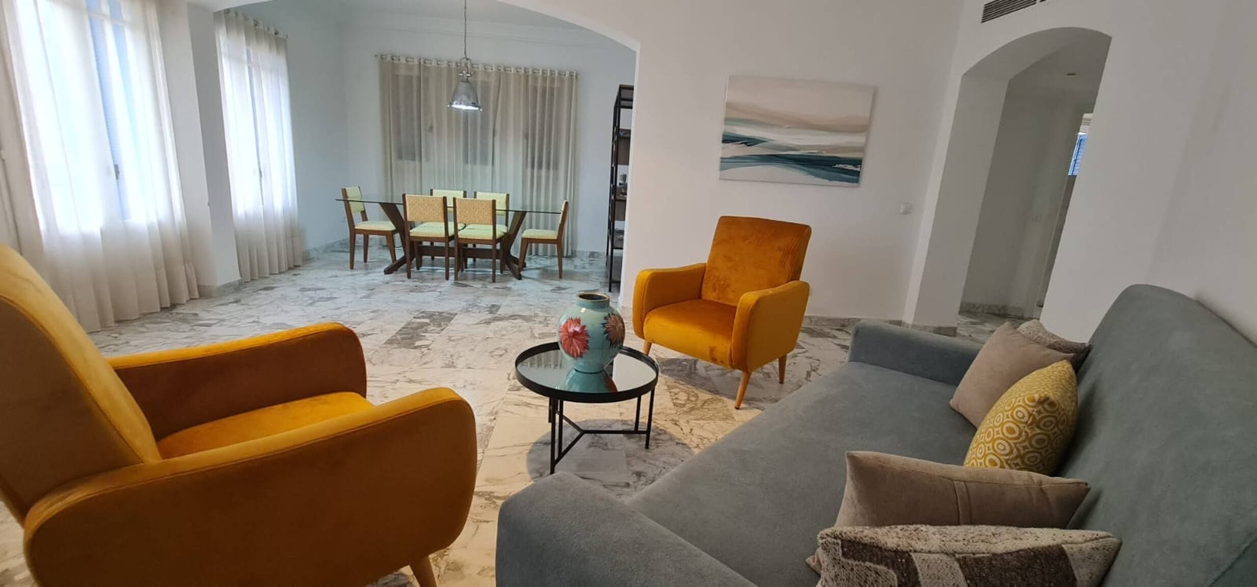 Una sala de estar con un sofá, dos sillones, una mesa de centro y una zona de comedor con sillas y una mesa.