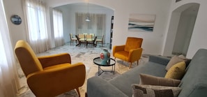 Una sala de estar con un sofá, dos sillones, una mesa de comedor con sillas y un florero sobre una mesita.