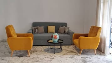 A living room with a marble floor, a grey sofa, two yellow armchairs, and a hanging light fixture.