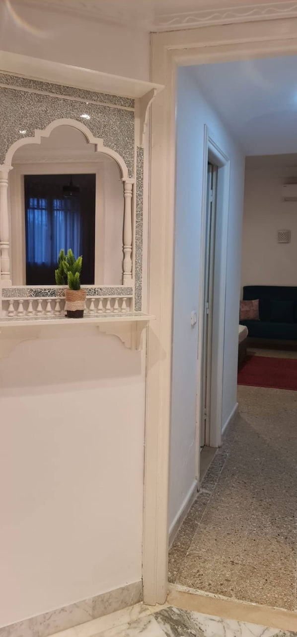 A hallway with a white wall, a marble floor, and a doorway leading to another room. - Horizon Bleu Apartment With Sea View (La Marsa)