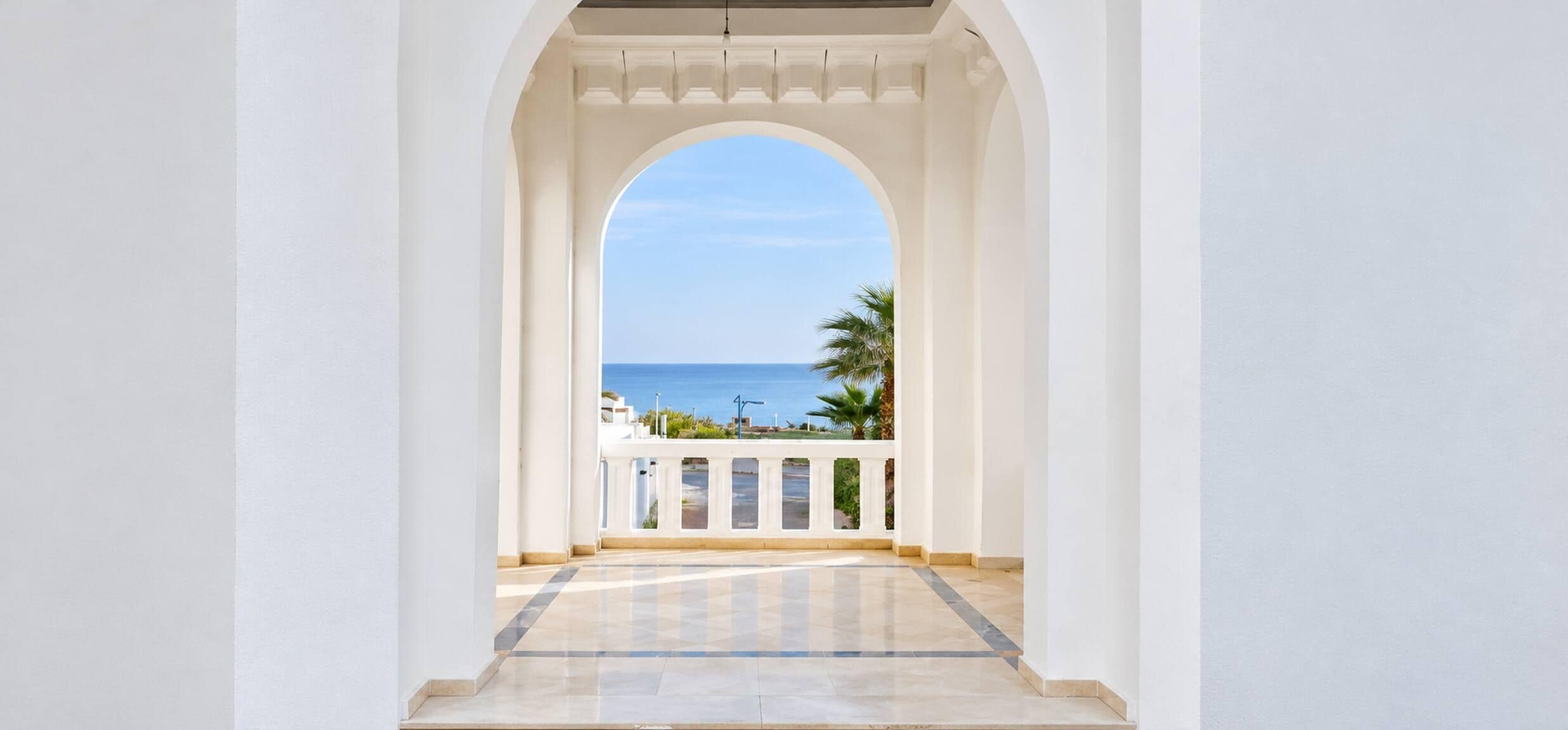 A corridor with a view of the sea and palm trees.