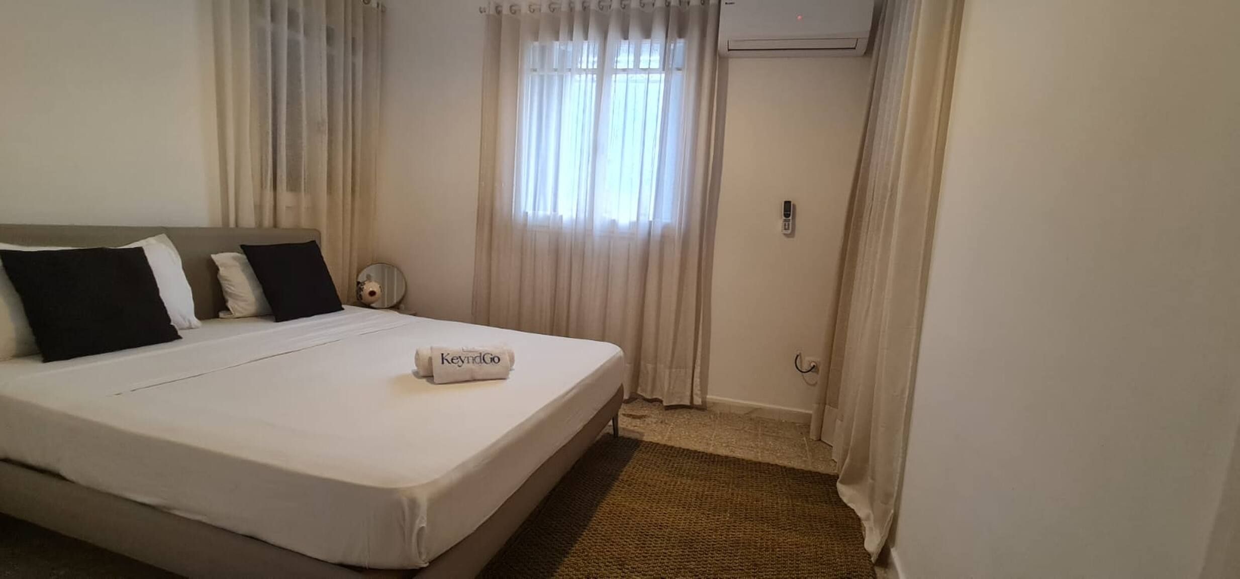 A hotel room with a bed, a bedside table, a mirror, and a window with curtains.