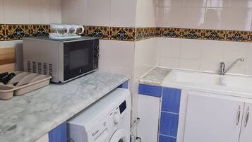 Una cocina compacta con armarios blancos, microondas, lavadora y fregadero.