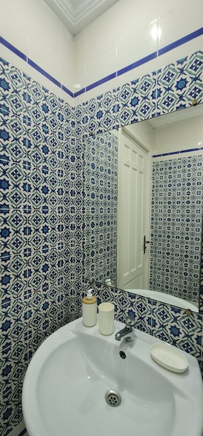 Un baño con un lavamanos blanco, un espejo y azulejos azules y blancos con estampado en las paredes.