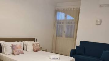 Un dormitorio con cama, un sofá azul, un tapete rojo y una ventana con cortinas.