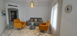 A living room with a sofa, two armchairs, a coffee table, and a hanging light fixture. - Horizon Bleu Apartment With Sea View (La Marsa)