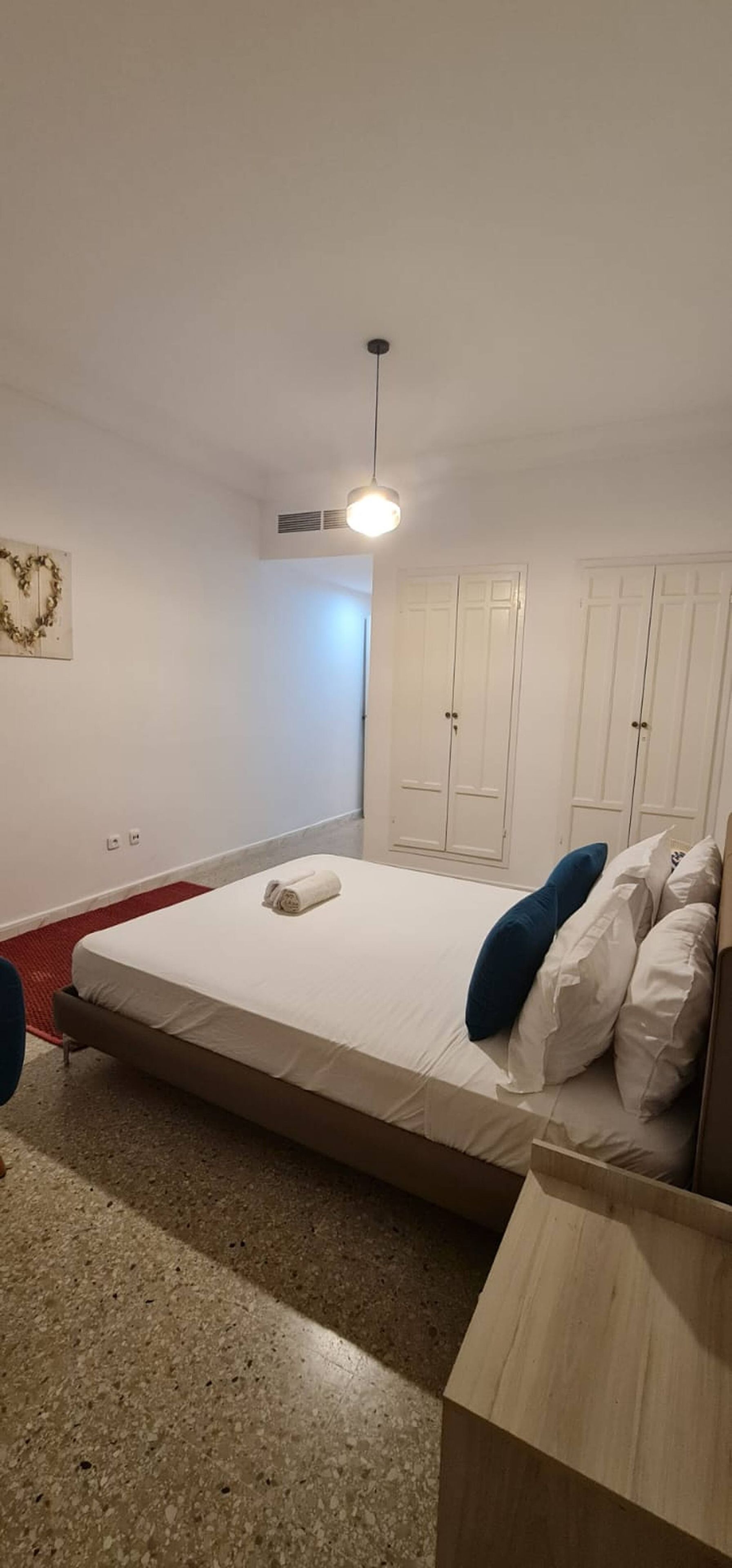 A bedroom with a bed, a wardrobe, a bedside table, and a hanging light fixture.